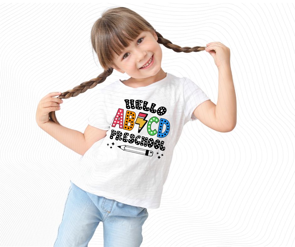 Young girl wearing a white t-shirt with Colorful ABCD with pencil lightning bolt image and bubble letter text "HELLO PRESCHOOL" image.