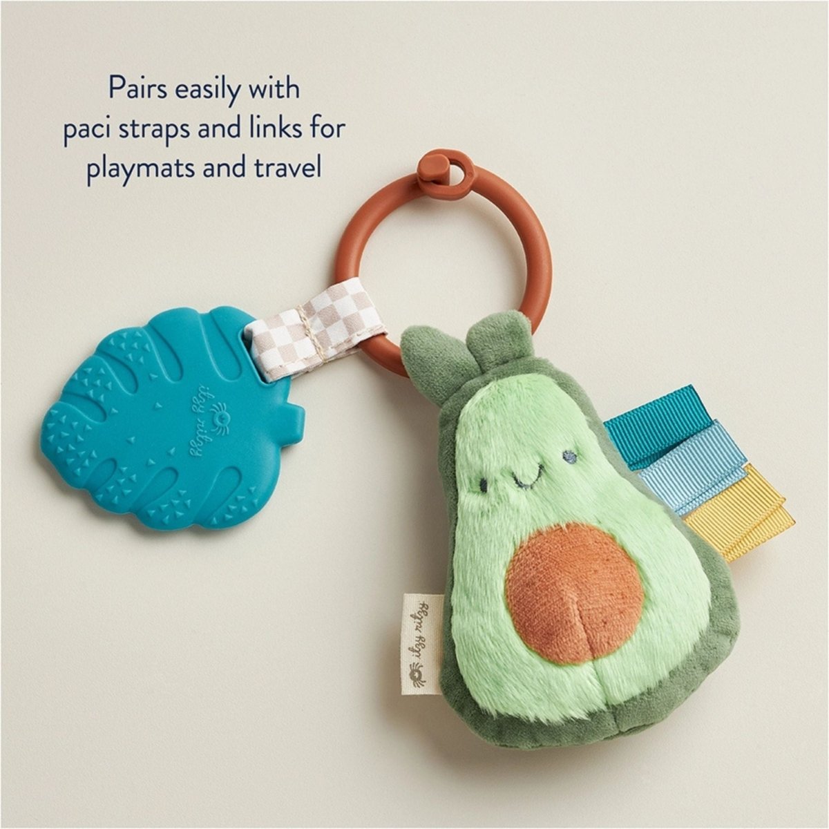 Avocado green plush sensory plush toy and teal leaf silicone teether set with clip on beige background.