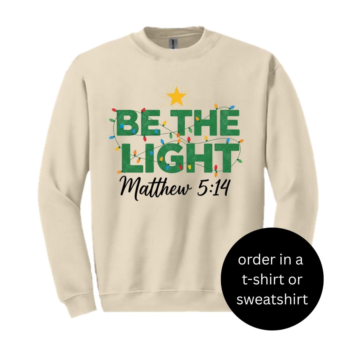 Beige sweatshirt with 'Be the Light Matthew 5:14' text and Christmas lights design. Sweatshirt sitting on white background.