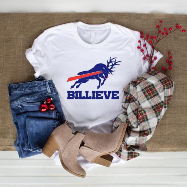 white tshirt with blue red Buffalo football reindeer design and BILLIEVE under it in blue text sitting on tan blanket with jeans, scraf, and boots. Little Gift Nook