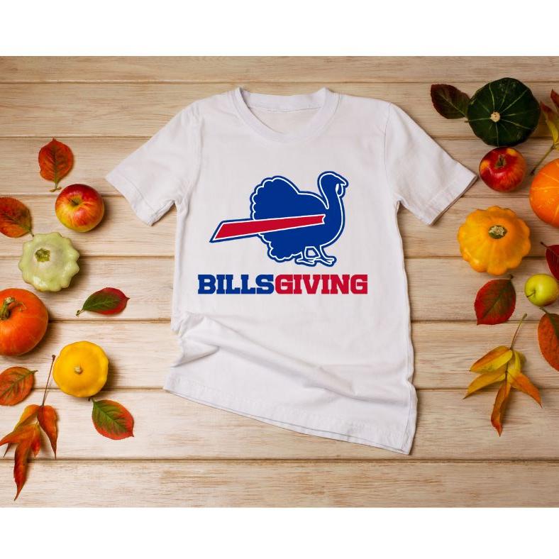 White BILLSGIVING Blue red turkey Buffalo football Thanksgiving tshirt laying on wood background with pumpkins.