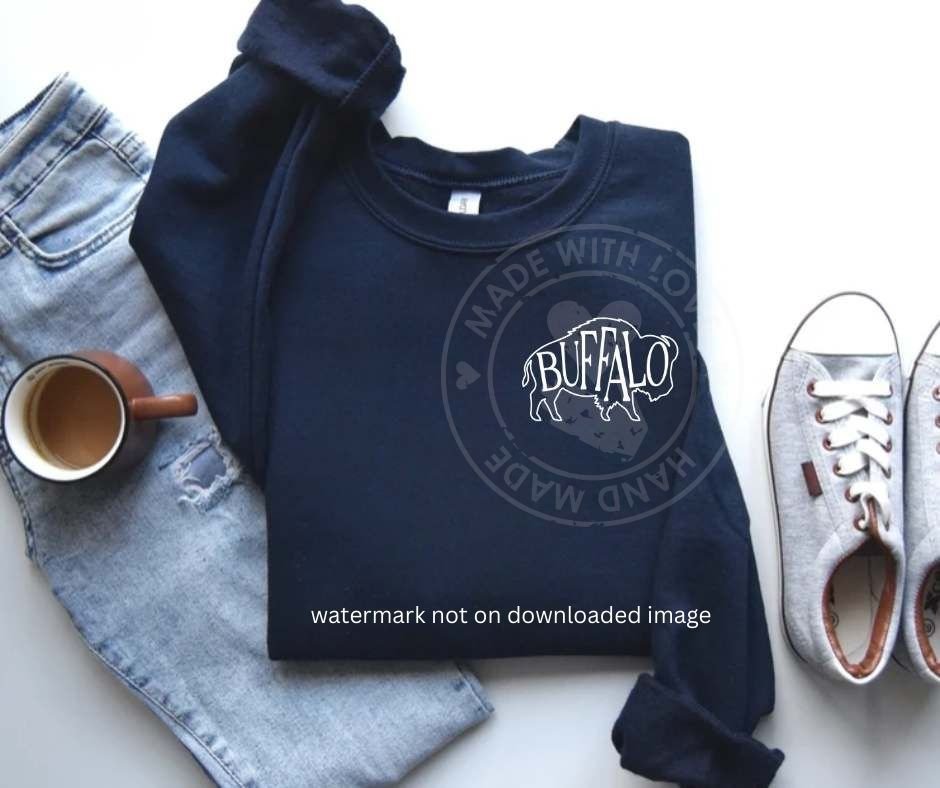 navy crewneck folded sweatshirt with white buffalo outline image and "BUFFALO" text inside on front of shirt on white background with jeans, shoes, and a coffee cup.