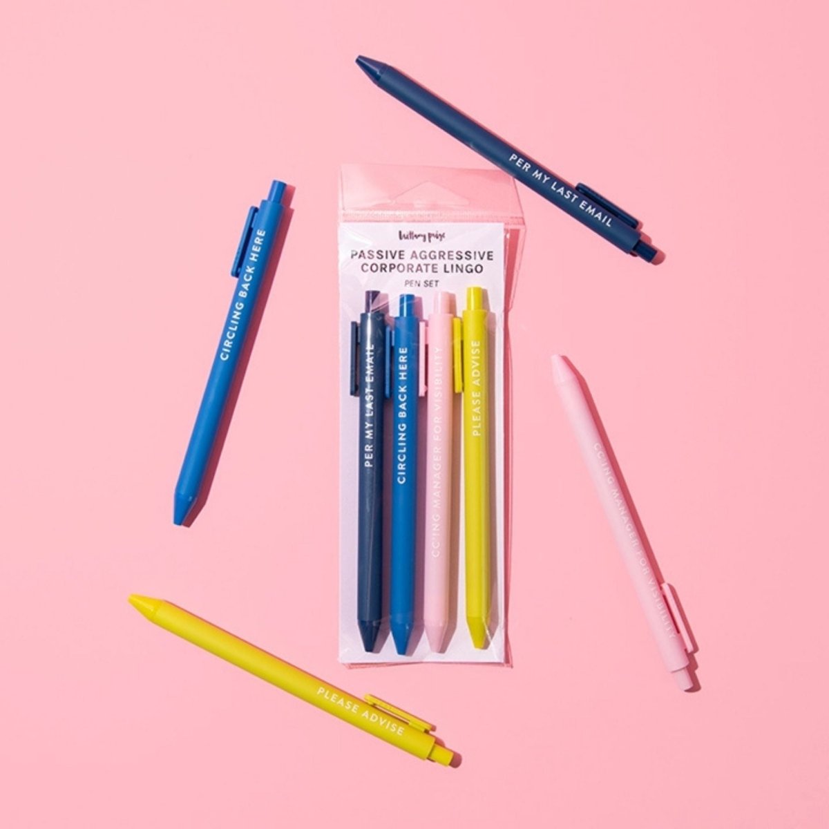 4 pack of colored corporate passive aggressive saying pens set on a pink background.