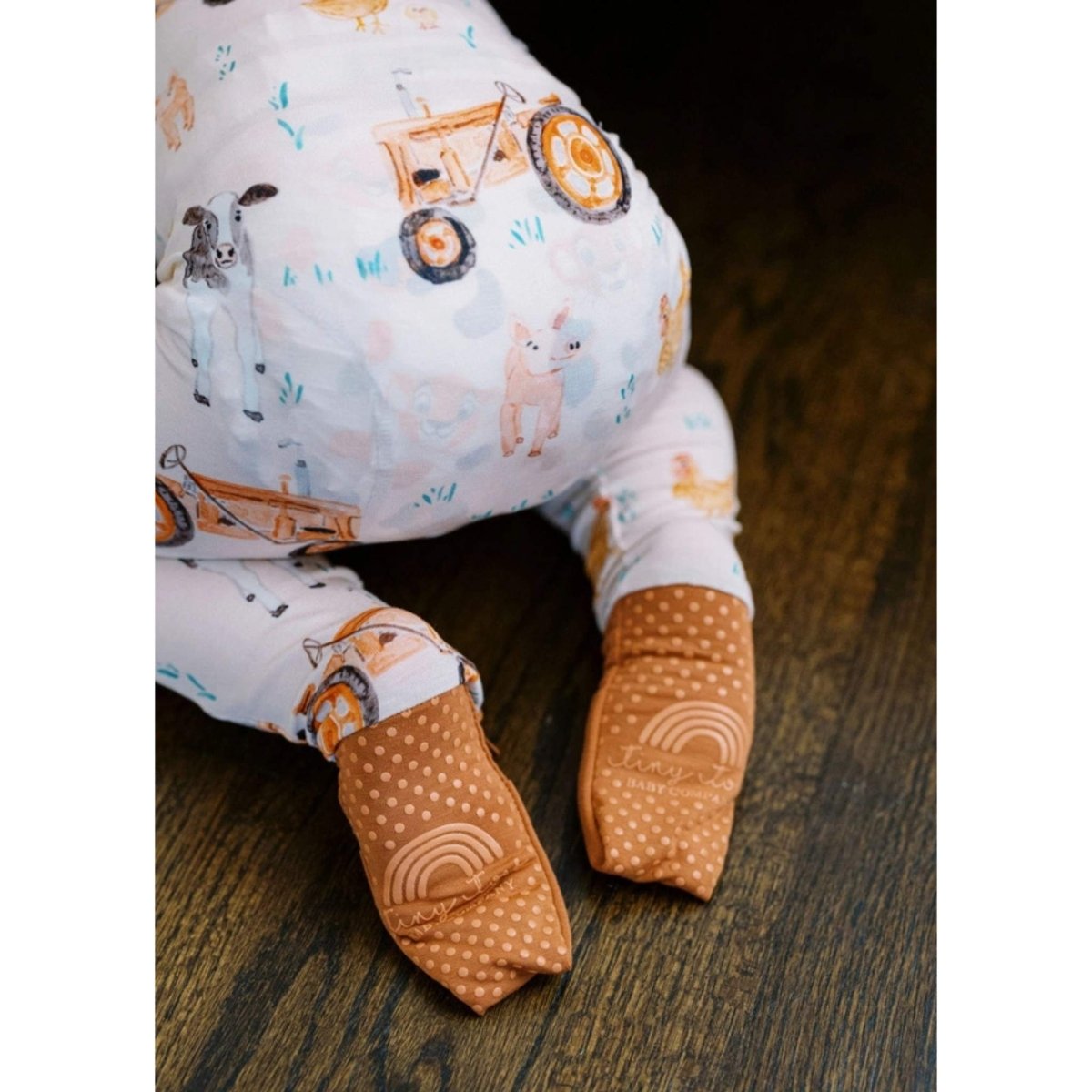 Farm theme bamboo baby sleeper back with fold over feet sitting on wood floor background.