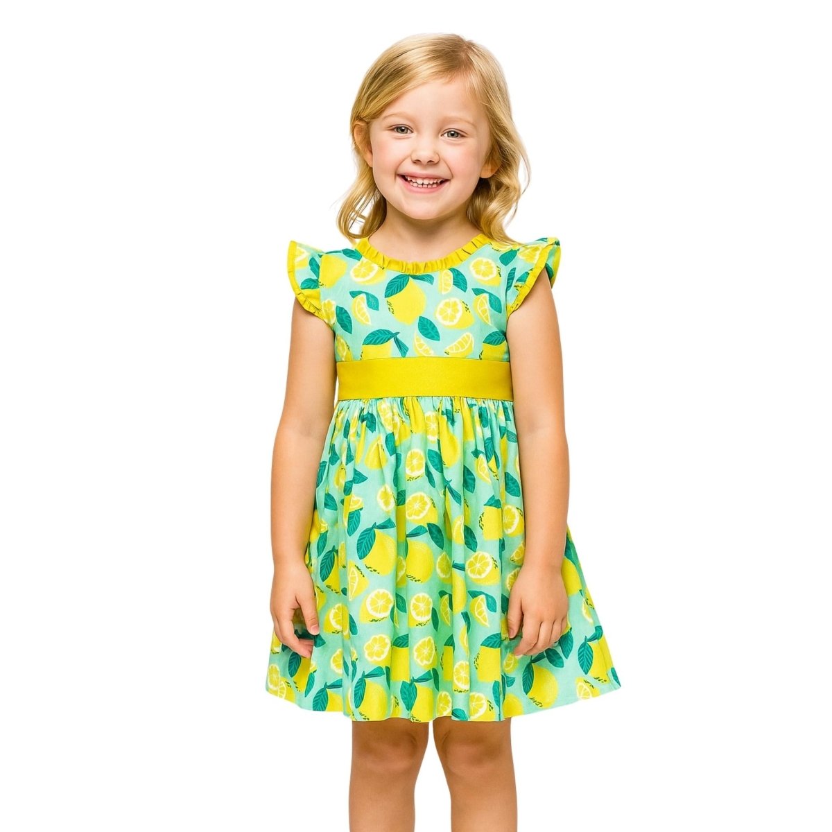 Little girl wearing yellow teal lemon print ruffle dress standing smiling.