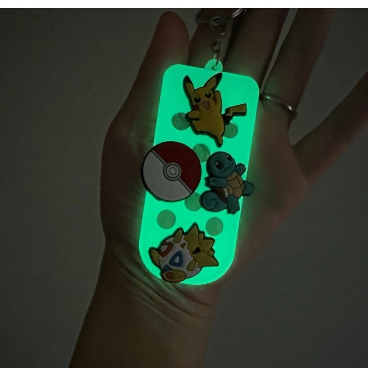 Glowing shoe charm keychain with character charms held in a hand against a dark background.