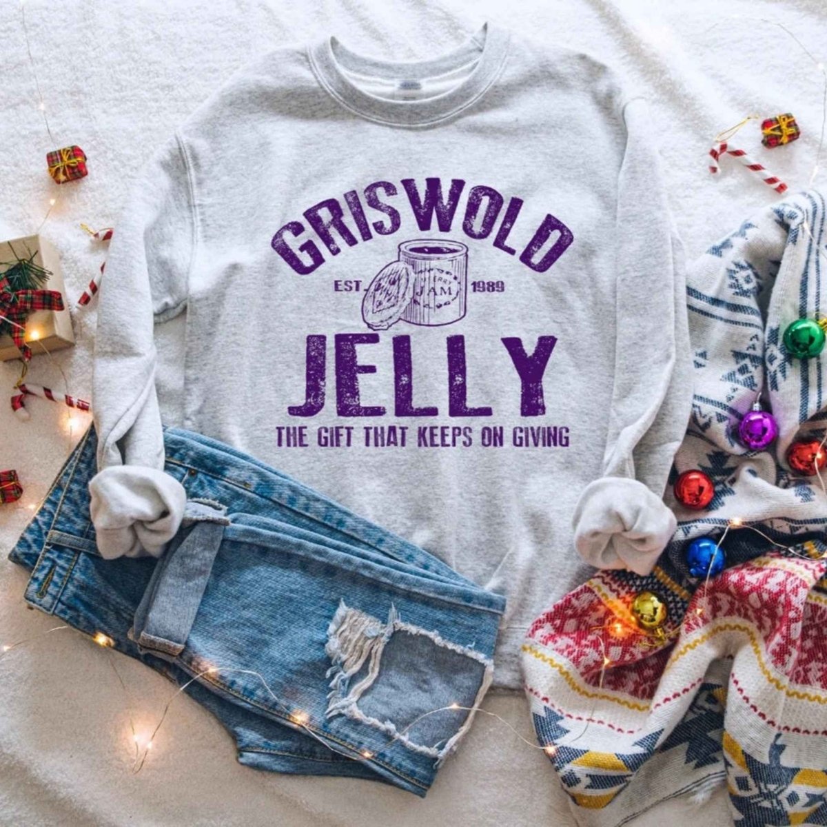 Heather gray and purple "Griswold Jelly of the Month Club" Crewneck Sweatshirt on christmas background with jeans. Little Gift Nook