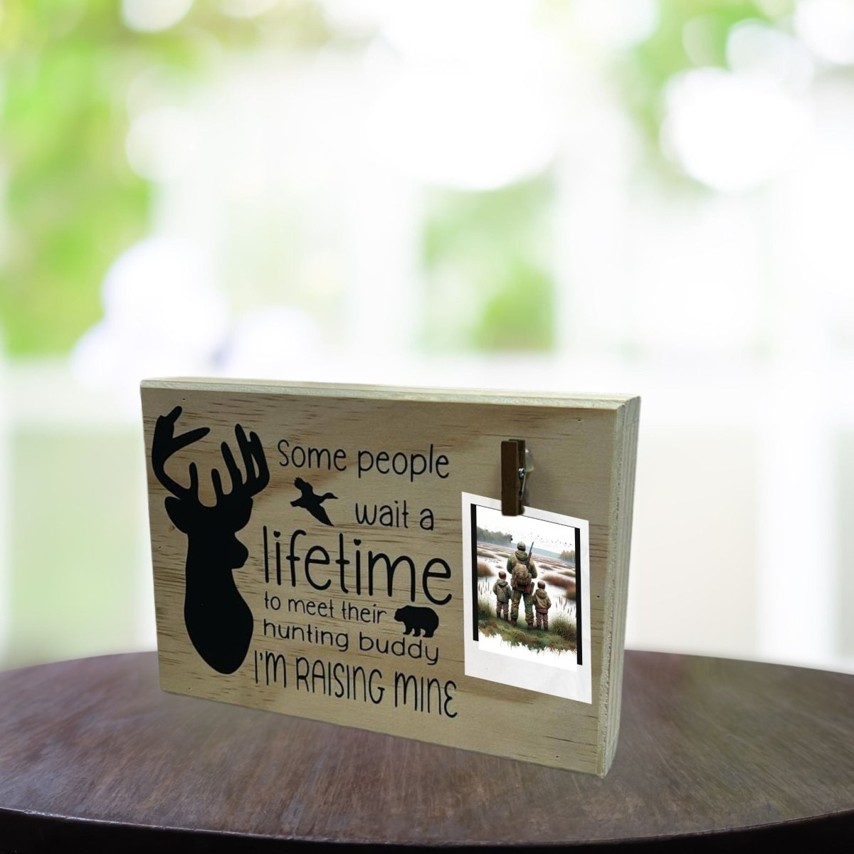 Hunting Buddy” Wooden Photo Clip Plaque - 9" x 6" x 1.5" wooden plaque with black vinyl lettering "some people wait a lifetime to meet their hunting buddy. I'm raising mine" with silhouette of buck deer and clip to hold photo - Little Gift Nook