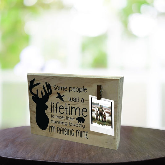 Hunting Buddy” Wooden Photo Clip Plaque - 9" x 6" x 1.5" wooden plaque with black vinyl lettering "some people wait a lifetime to meet their hunting buddy. I'm raising mine" with silhouette of buck deer and clip to hold photo - Little Gift Nook