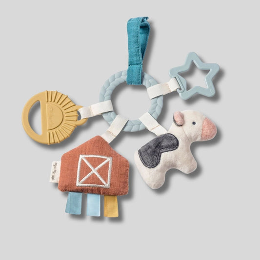 Itzy Ritzy Busy Ring Farm Teething Toy with silicone textured teethers, plush jingle cow, soft taggy sensory farm, and hook to attach to car seat or stroller. Shown on gray background - Little Gift Nook