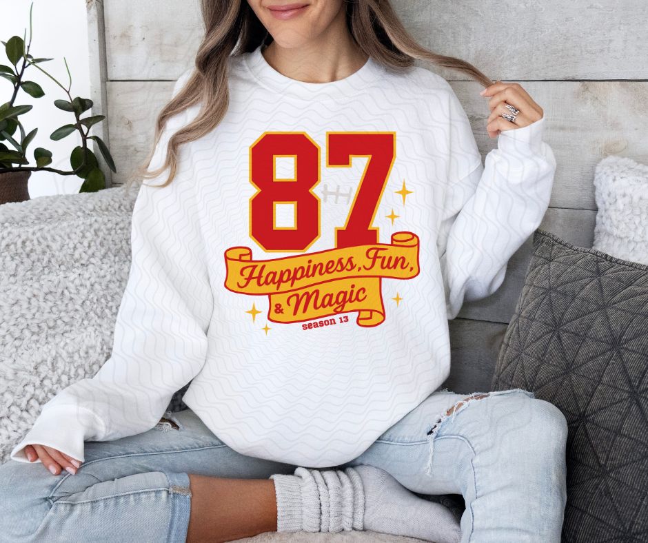 woman wearing white sweatshirt with red yellow 87 Happiness, fun, magic season 13 on front. KC Football digital image.