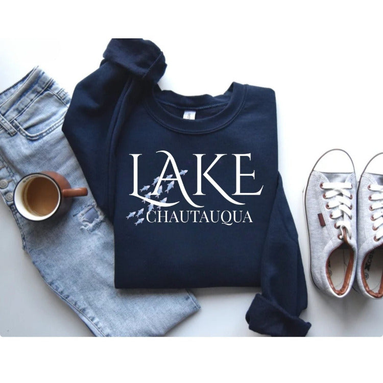 Folded Lake Chautauqua navy sweatshirt with white text and blue fish graphic, styled with sneakers, jeans, and coffee – Little Gift Nook