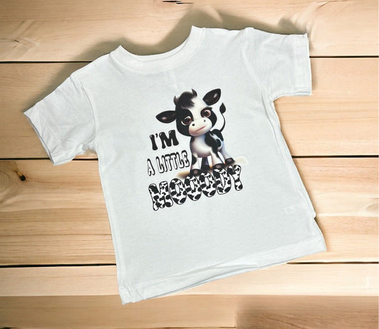 White toddler tshirt with black white cow and "I'm a Little Mooody" on front sitting on wood background. Little Gift Nook