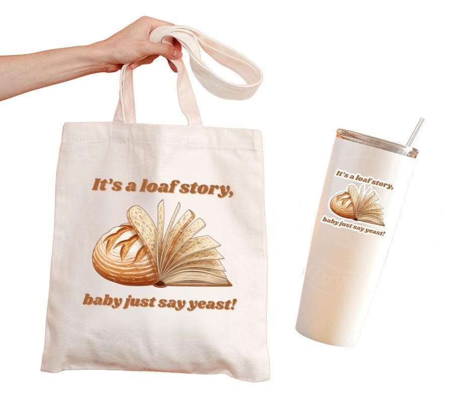 beige tote bag and tumbler with image of sourdough loaf with slices pages of book image with tan text "It's a loaf story, baby just say yeast" on fronts as decals or stickers.