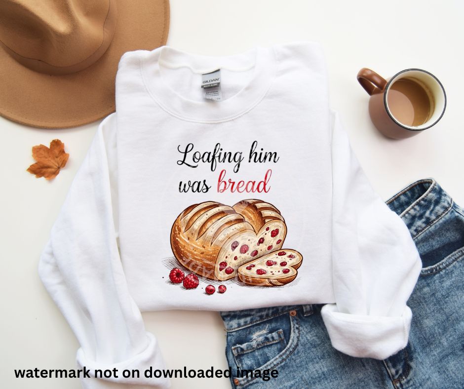 white folded sweatshirt with image of sourdough loaf shaped like heart with red berries in it and beside it text "loafing him was bread" on front with jeans, hat, and coffee cup on white background.