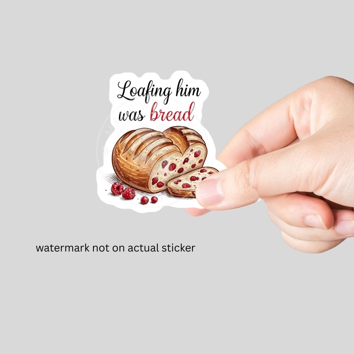 hand holding sticker of "Loafing him was bread heart shapped sourdough loaf with red berries on white background.