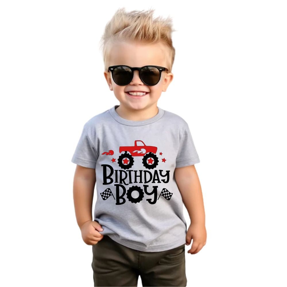 Child in sunglasses and wearing a gray t-shirt with 'Birthday Boy' and a red monster truck graphic on front standing on white background.