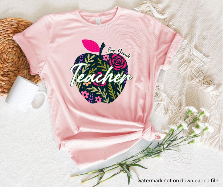 Pink tshirt with navy floral apple 3rd grade teacher image on front laying flat on white background with flowers.