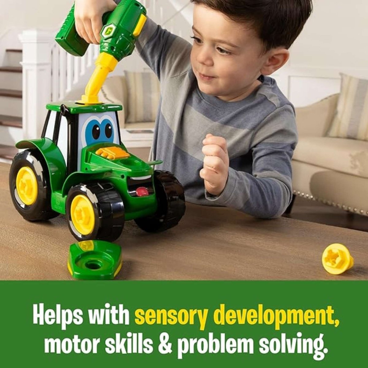 Child putting together a John Deere plastic tractor toy with toy drill on brown table top.