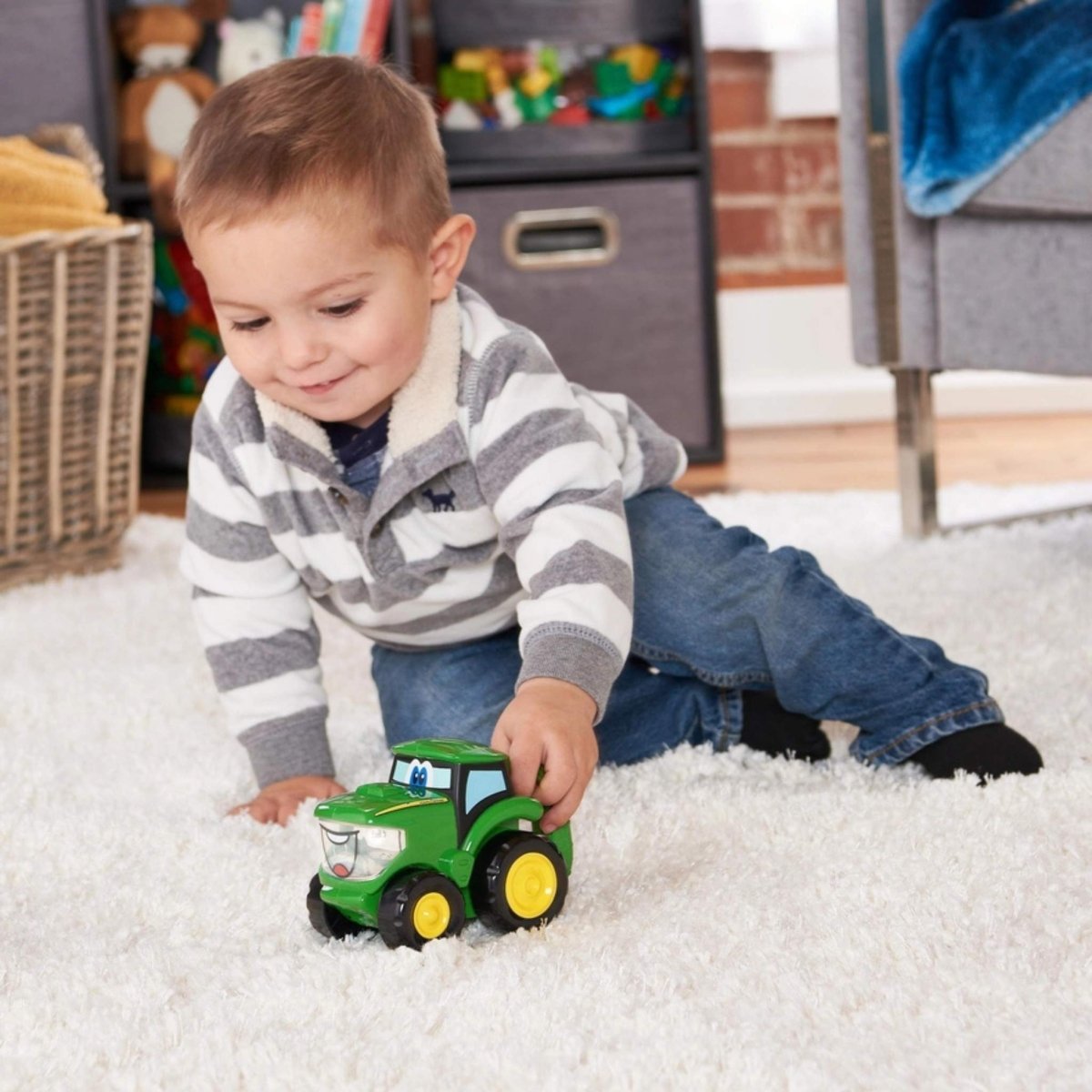 Little boy playing with John Deere TOMY toy tractor flashlight on white fuzzy rug.