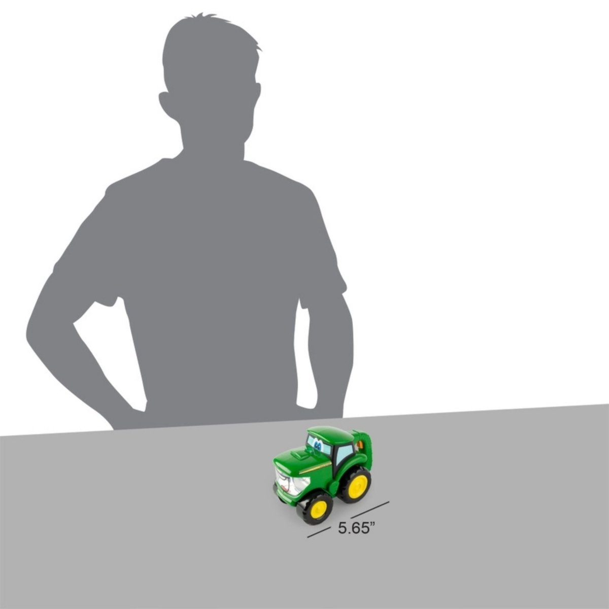 John Deere TOMY toy tractor flash light measuring 5.65" on gray surface with man silhouette standing next to.