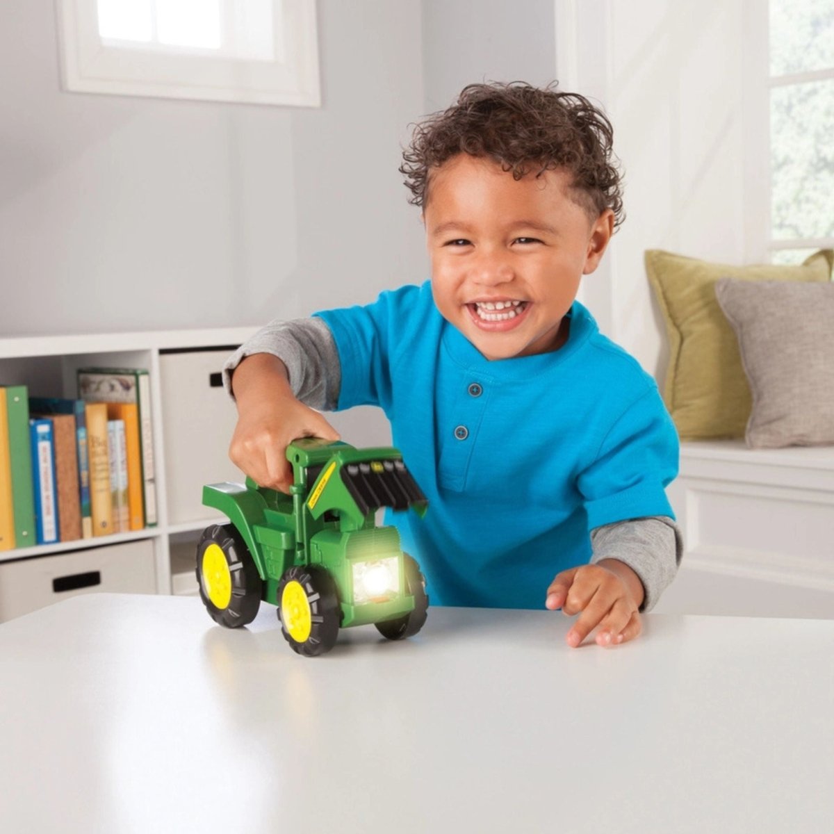 little boy playing with push n go Tomy John Deere flashlight toy on white table.