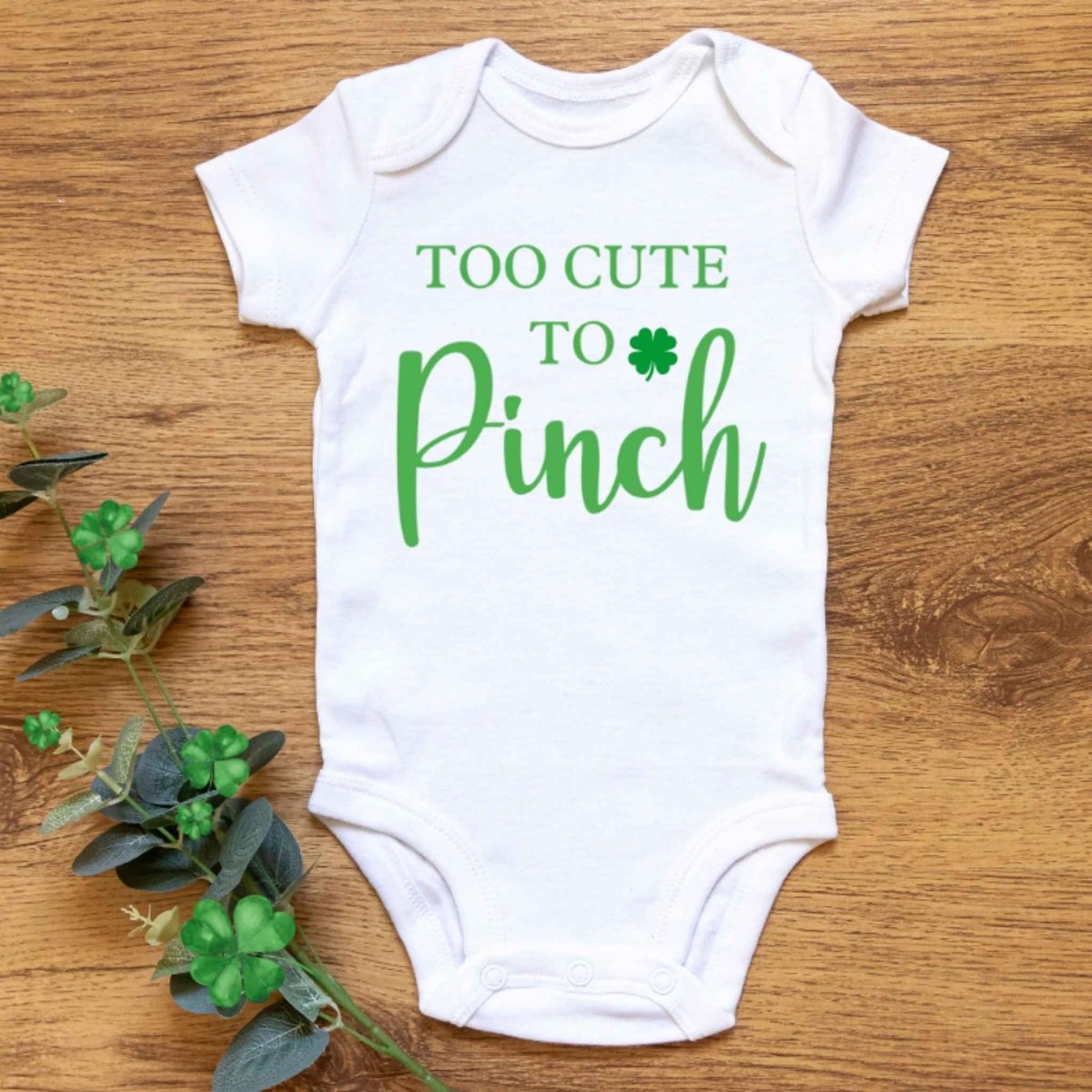 white green too cute to pinch clover baby onesie on wood background with clover greenery - Little Gift Nook