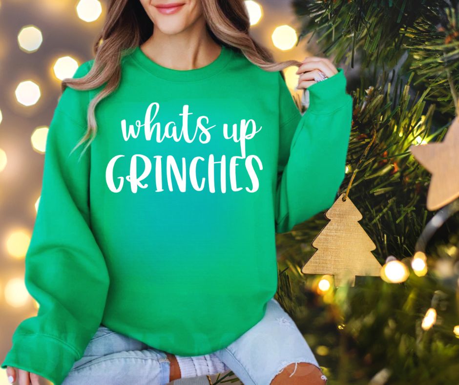 woman wearing green sweatshirt with "whats up grinches" in white on front sitting in front of tree.