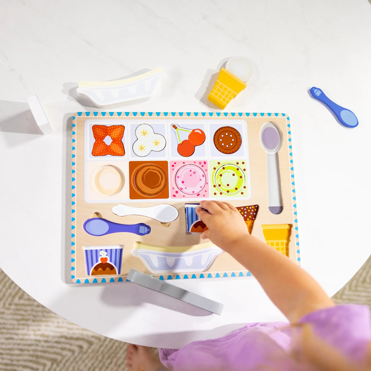 child playing with wooden magnetic ice cream puzzle and play set on white table background.