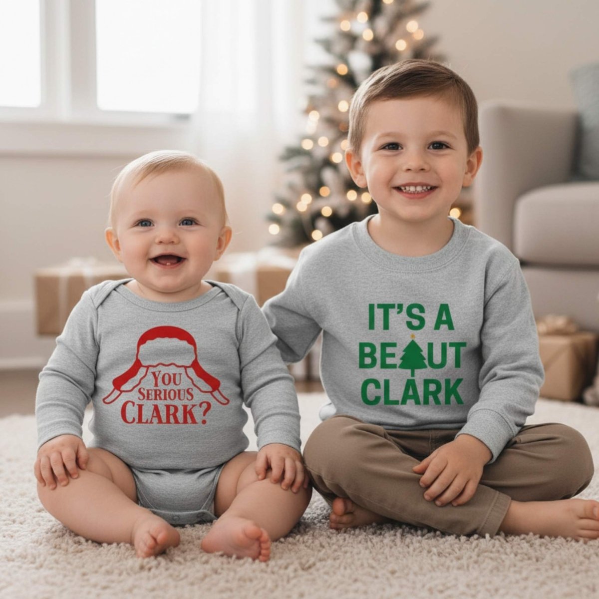 Baby wearing gray are you serious Clark onesie and little boy wearing gray it's a beaut Clark sweatshirt sitting on white rug on Christmas background.