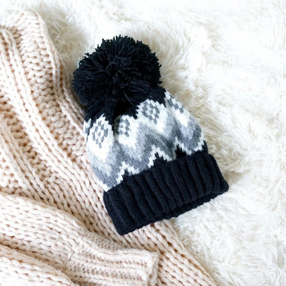 Aztec knit lined black pom hat on white fur background.
