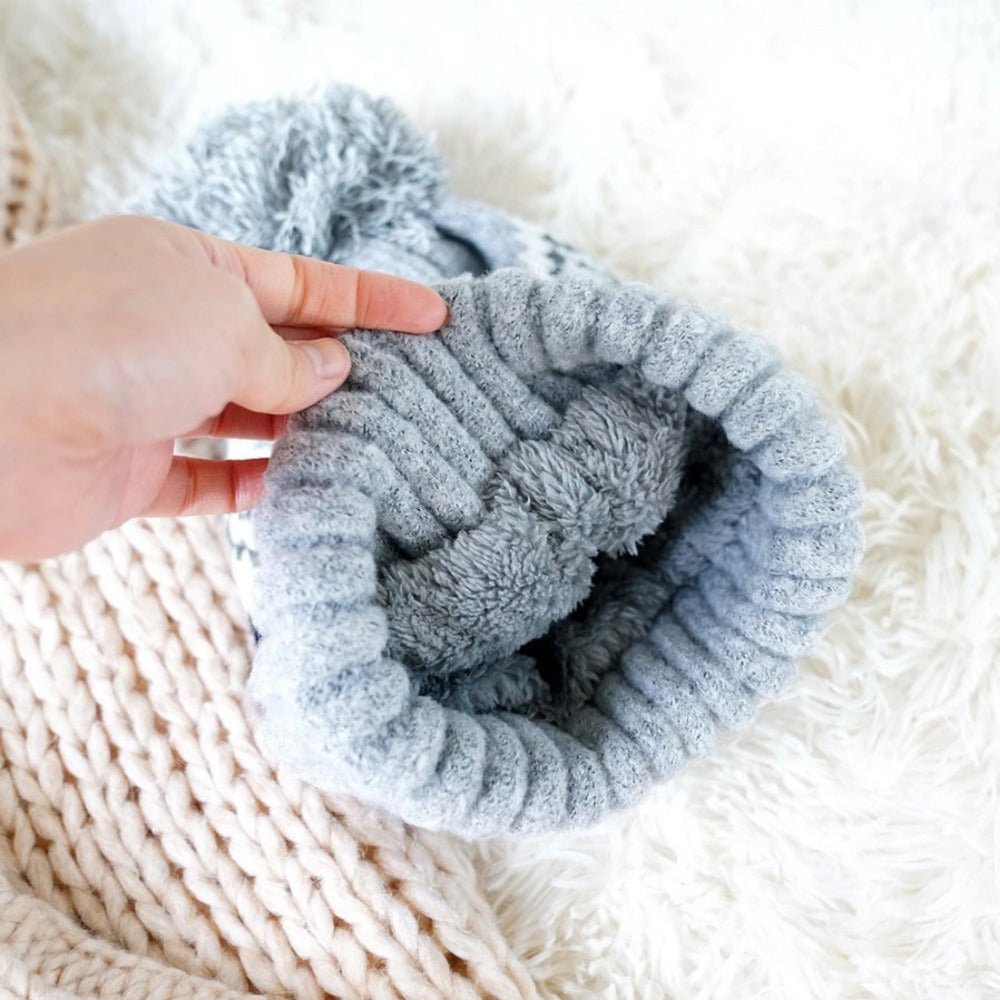 Gray aztec knit lined pom hat on white fur background.