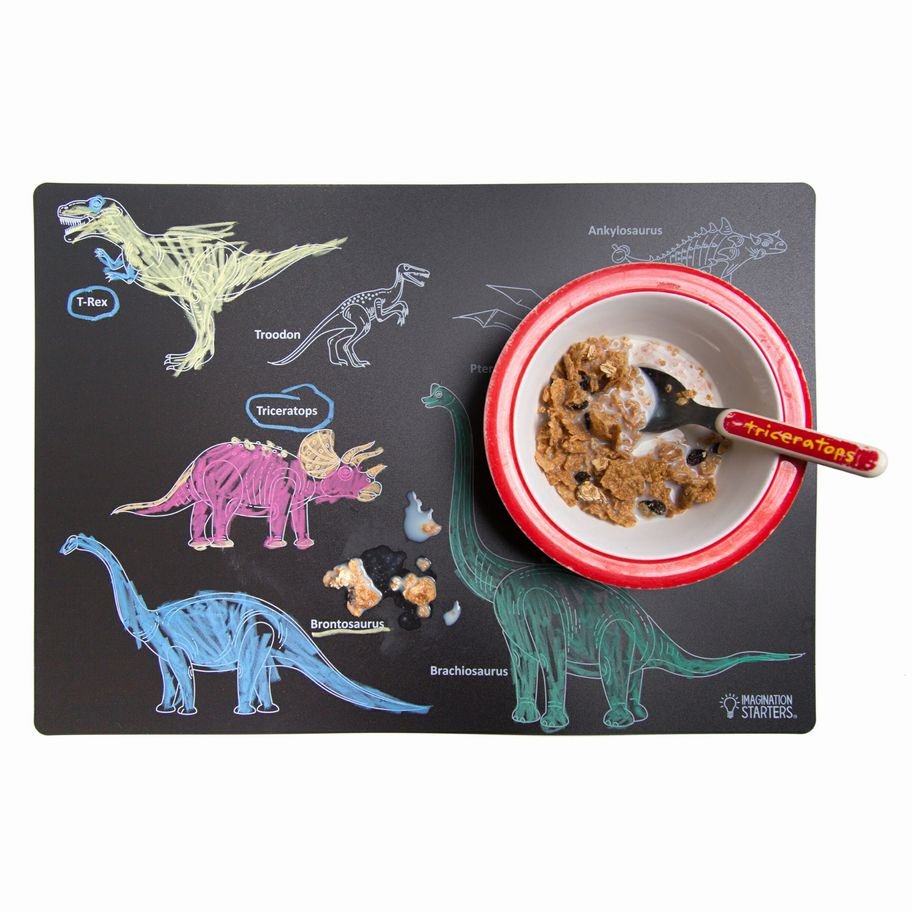 Imagination Starters Dinosaur wipe off black plastic Reusable Placemat with dinosaurs colored in with crayons and a cereal bowl sitting on top on a white background.