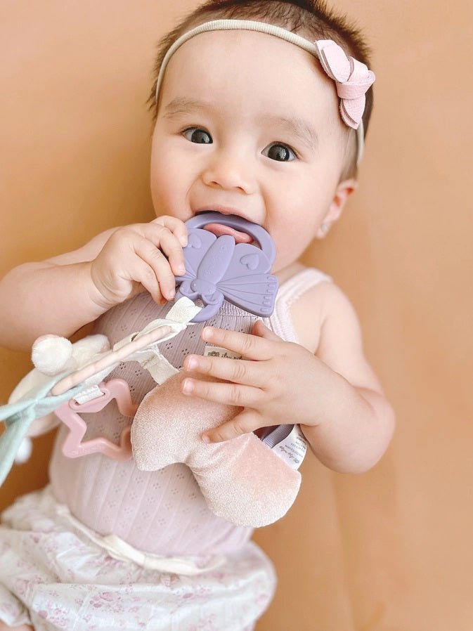 Baby holding Itzy Ritzy Bitzy Busy bunny Ring butterfly teether on orange background.