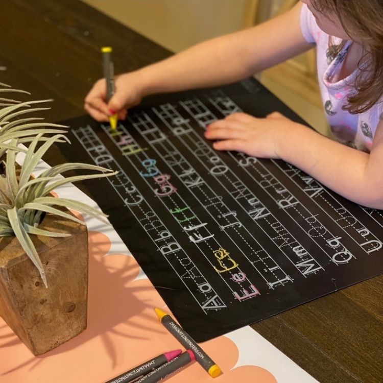 little girl writing alphabet on learning mat with wipe off crayons.