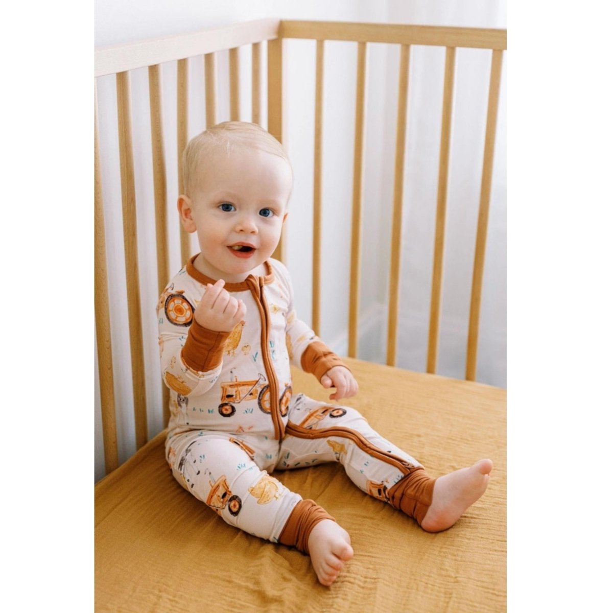 baby in tractor bamboo sleeper sitting in crib.