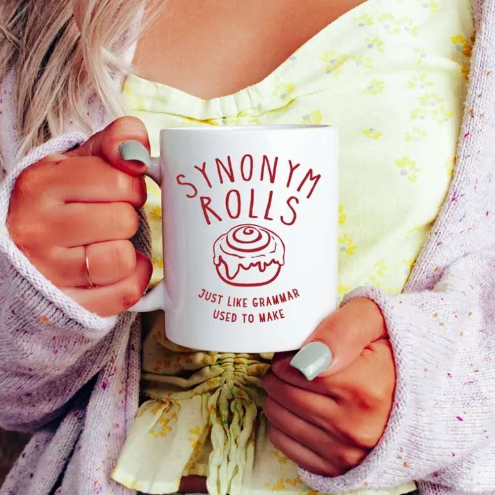 woman holidng mug with "synonym rolls just like grammar used to make" on front.