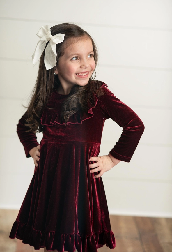 Burgundy Velvet Twirl Holiday Dress. Little Girl modeling dress with hair bow. Little Gift Nook.