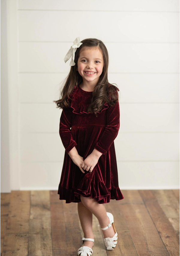 Burgundy Velvet Twirl Holiday Dress. Long Sleeve with ruffles on front. Soft & stretchy. Little Girl modeling dress. Standing in dress. Little Gift Nook.