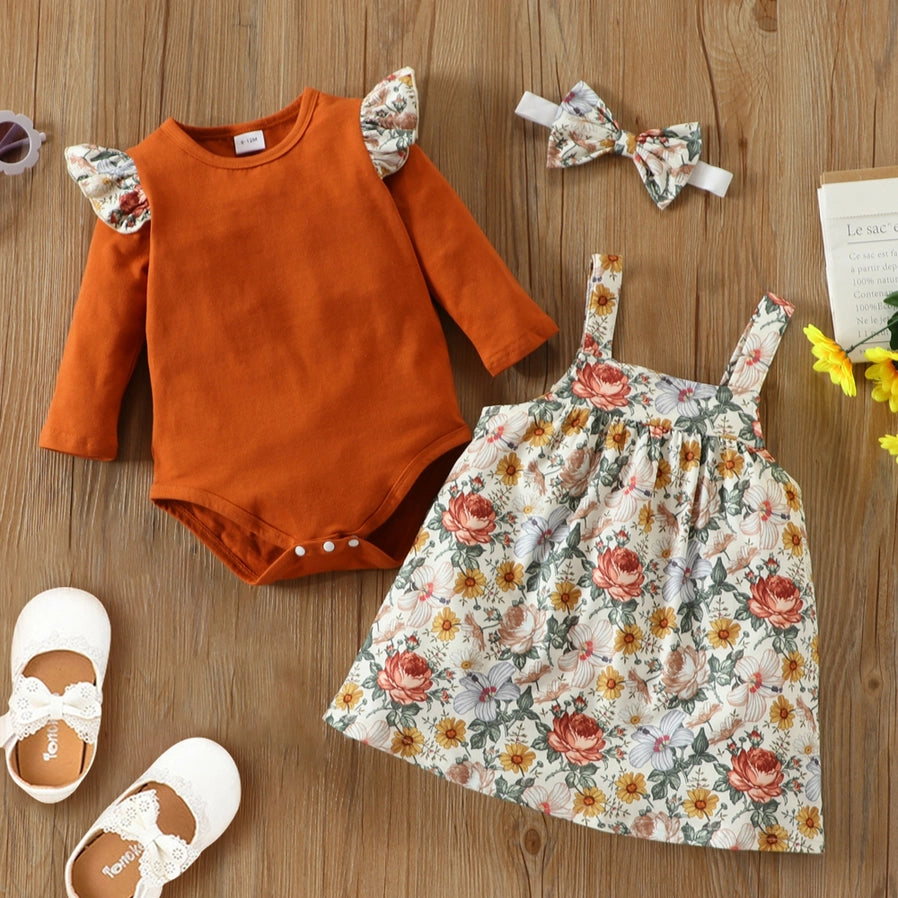 Floral Baby Girl 3pc Jumper Dress Set. Marigold, orange, white floral print with greenery soft jumper dress with orange long sleeve ruffle bodysuit for baby girl.  3 piece set layed out. Bodysuit snaps. Shoes not included. 