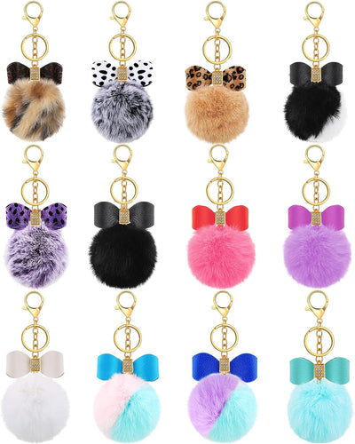 Fluffy Pom Pom Bow Keychains in various colors with gold color keyring and lobster clip.  Each soft fluffy pom pom ball has a faux leather bow and gems at top. Little Gift Nook.