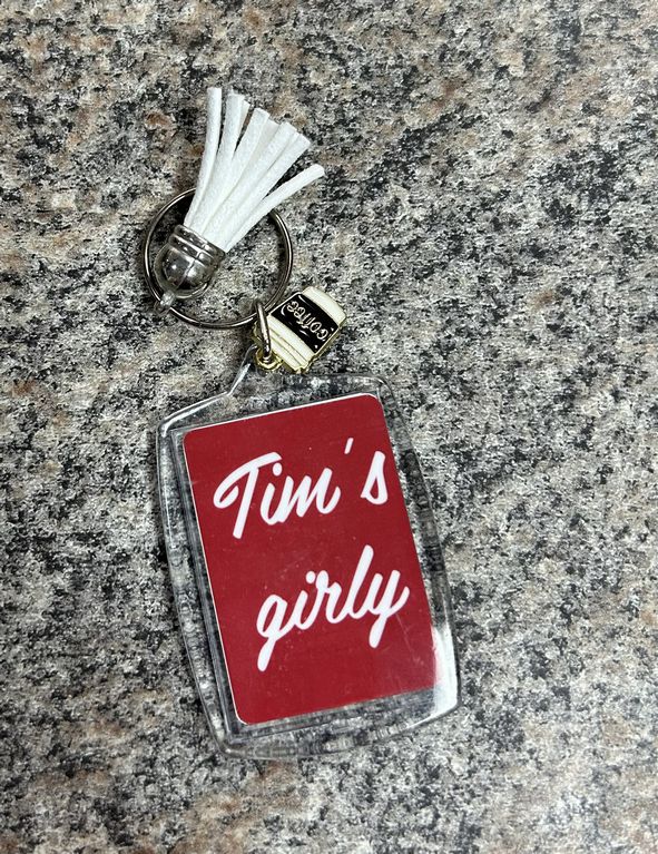 Tim's Girly Coffee Keychain. 2 inch tall rectangular clear double image keychain. One side is red with Tim's girly in white lettering. Other side is white with little red coffee cup with face. Comes with white tassel and metal coffee cup charm.- Little Gift Nook