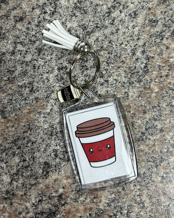 Tim's Girly Coffee Keychain. 2 inch tall rectangular clear double image keychain. One side is red with Tim's girly in white lettering. Other side is white with little red coffee cup with face. Comes with white tassel and metal coffee cup charm.- Little Gift Nook