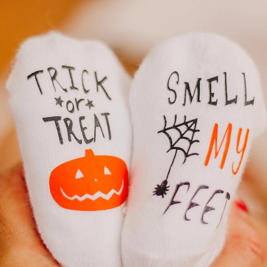 Trick or Treat Smell My Feet Baby Socks. White baby socks with bottoms of socks have pumpkin and spider image with lettering. - Little Gift Nook