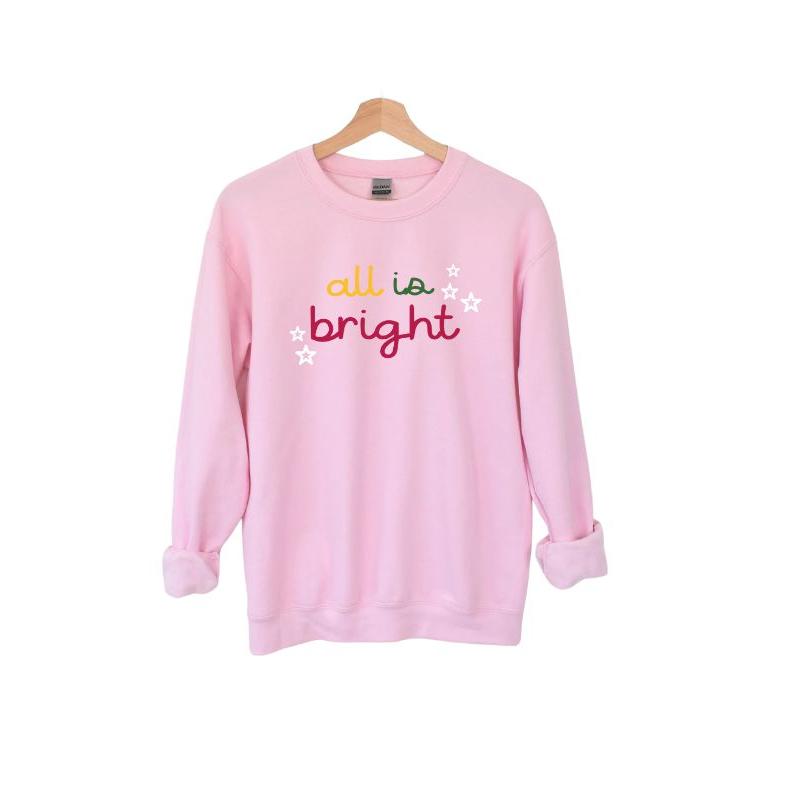 Pink "all is bright" yellow, green, and pink lettering with white stars sweatshirt hanging on wooden hanger on white background. 