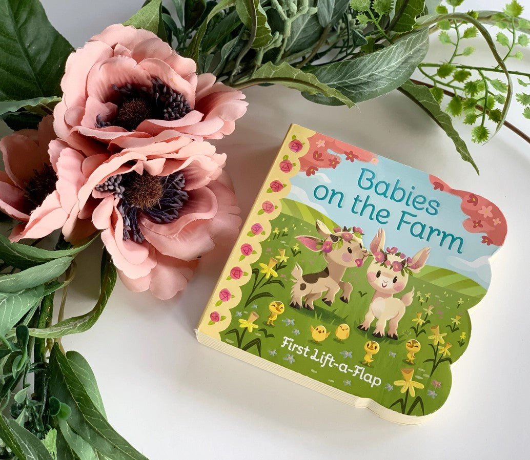 Babies on the farm lift the flap baby board book laying flat next to flowers. 