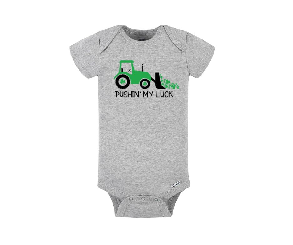 Gray baby onesie with green tractor, clovers, pushing my luck on front sitting on white background.