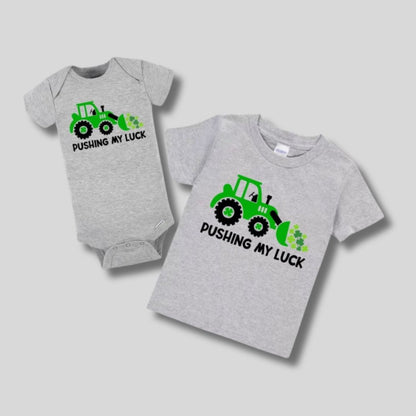gray baby onesie and kids tshirt with green tractor and clovers "pushing my luck" tshirts. On gray background. Little Gift Nook