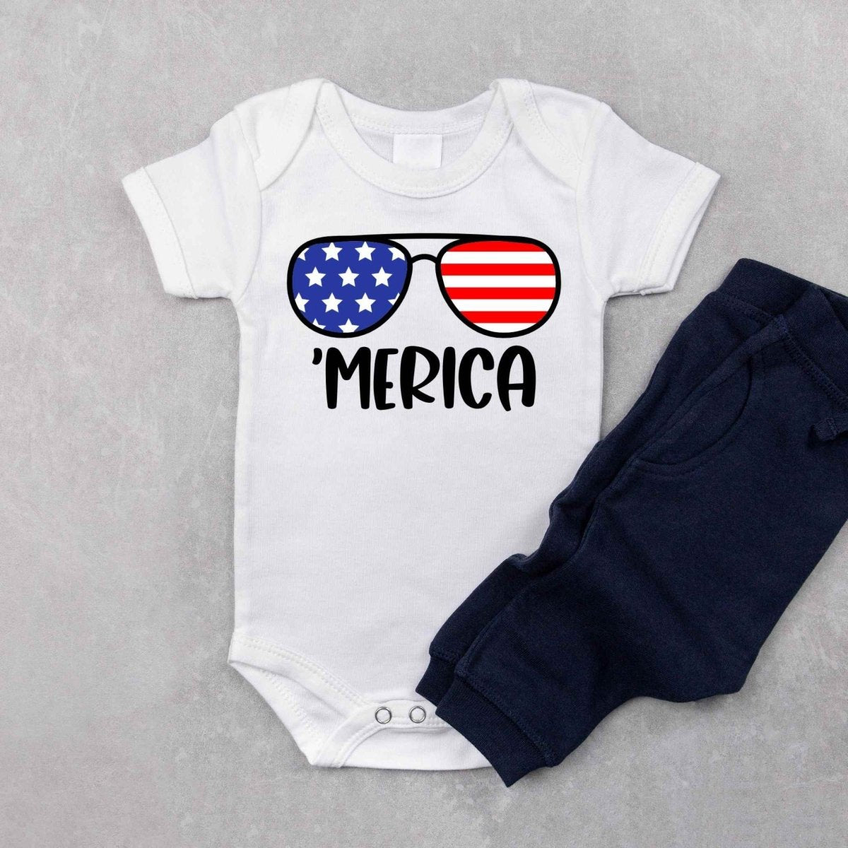 White onesie with red blue stars and stripes sunglasses and 'MERICA in black text on front with navy sweatpants - Little Gift Nook