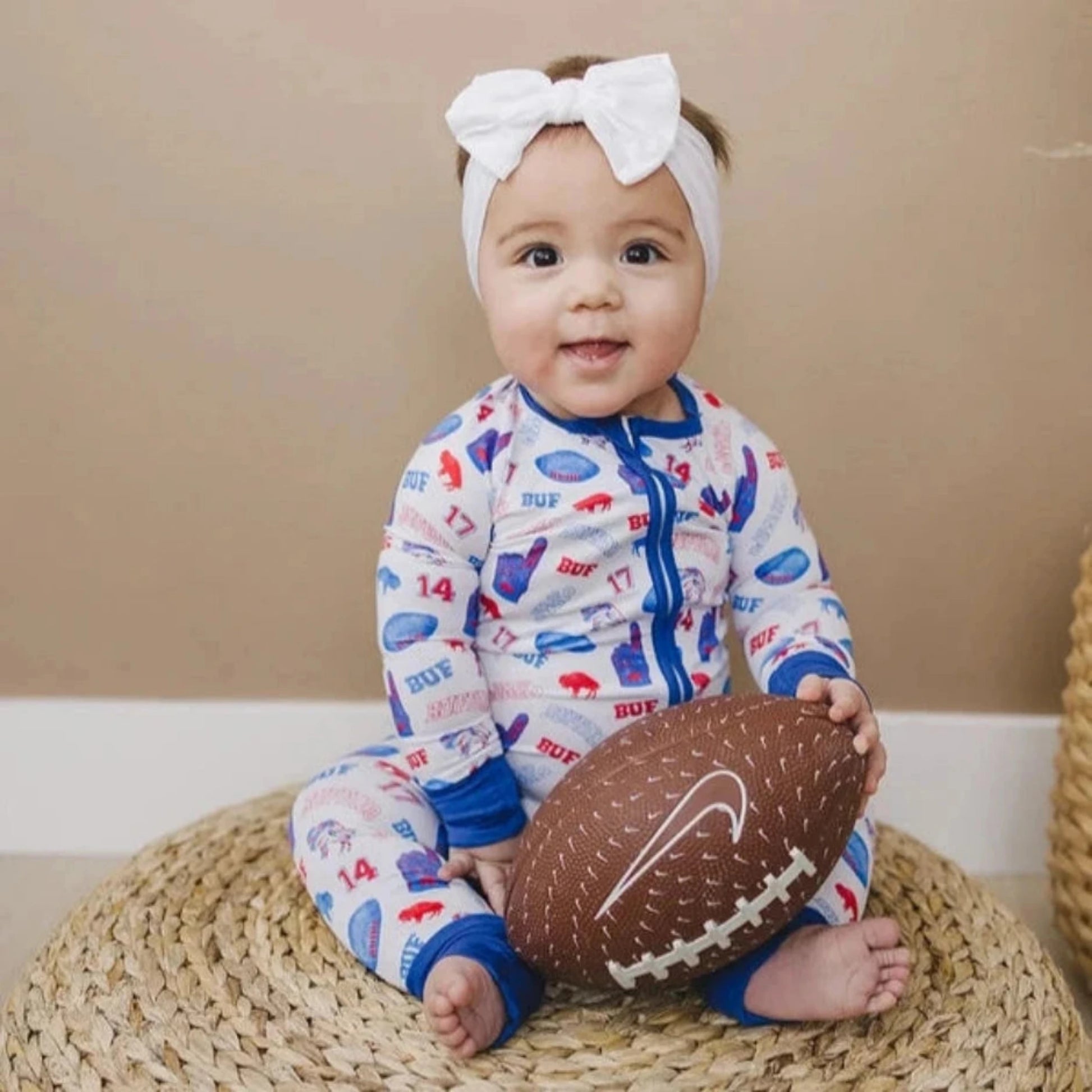Baby wearing white, royal blue, and red buffalo print sleeper with #17 and 86 print and holding football. Little Gift Nook